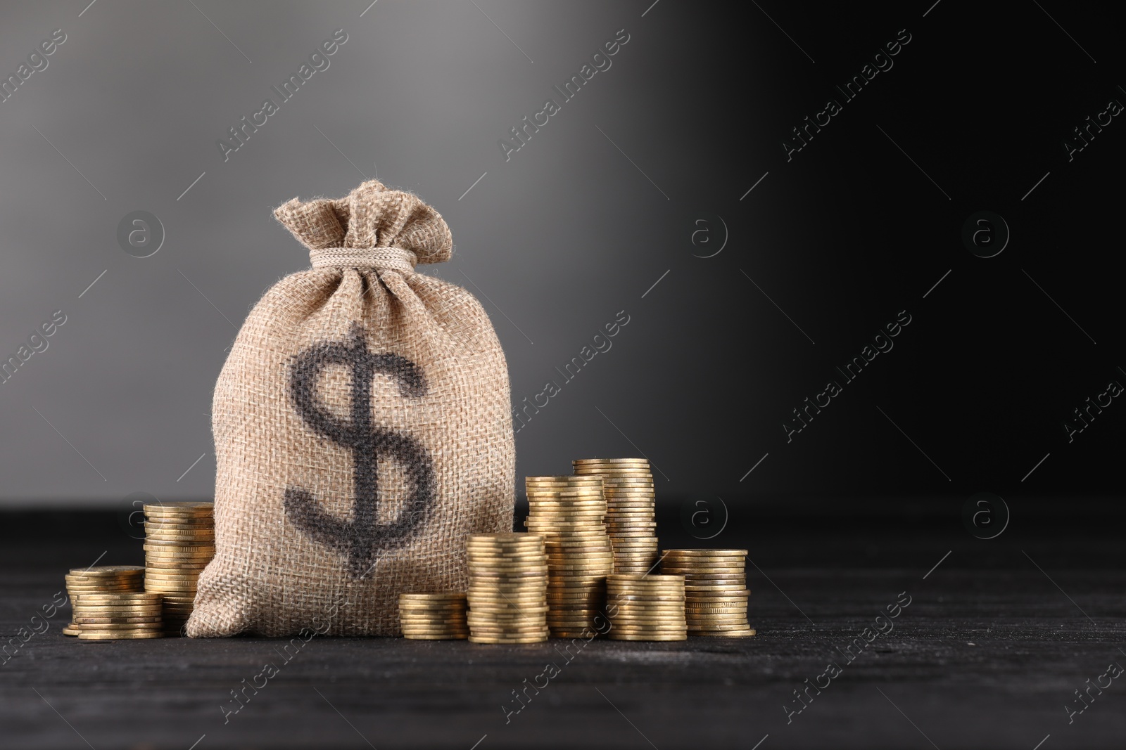 Bag with dollar sign and stacked coins on black table against gray gradient background, space for text Photo of Bag with dollar sign and stacked coins on black table against gray gradient background, space for text