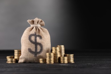 Photo of Bag with dollar sign and stacked coins on black table against gray gradient background, space for text