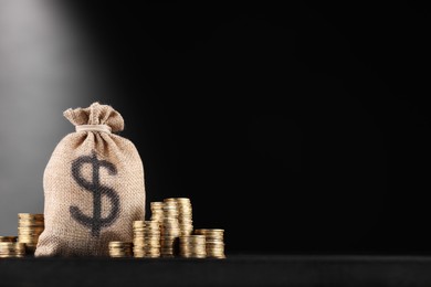 Photo of Bag with dollar sign and stacked coins on black table against dark gradient background, space for text