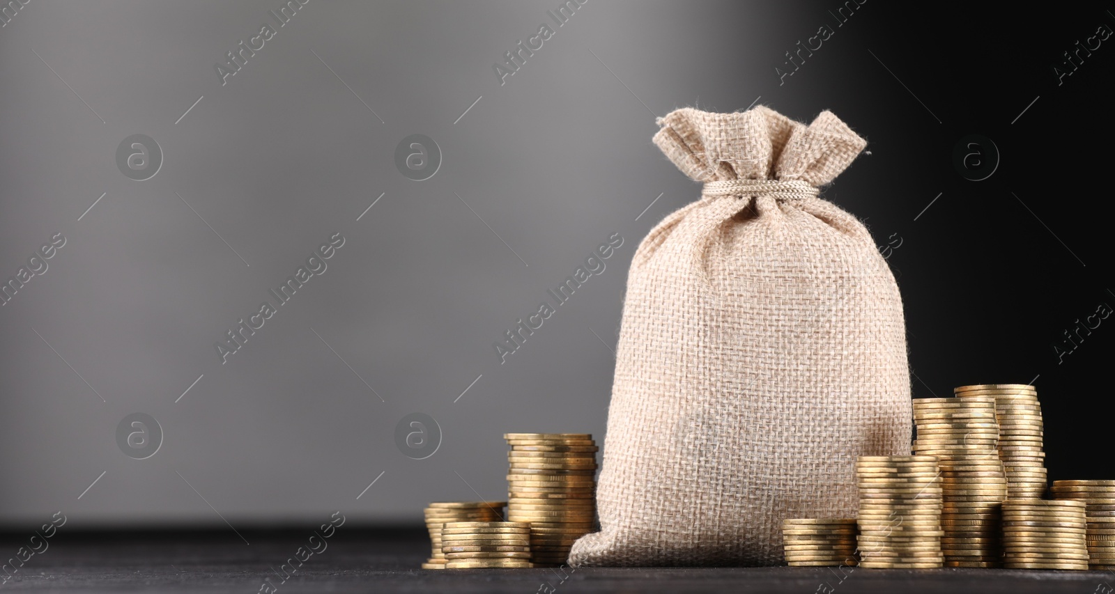 Bag and stacked coins on black table against gray gradient background, space for text Photo of Bag and stacked coins on black table against gray gradient background, space for text