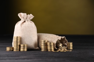 Photo of Bags and stacked coins on black table against dark yellow background