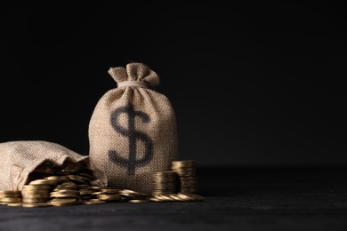 Photo of Bags with dollar sign and coins on dark background, space for text
