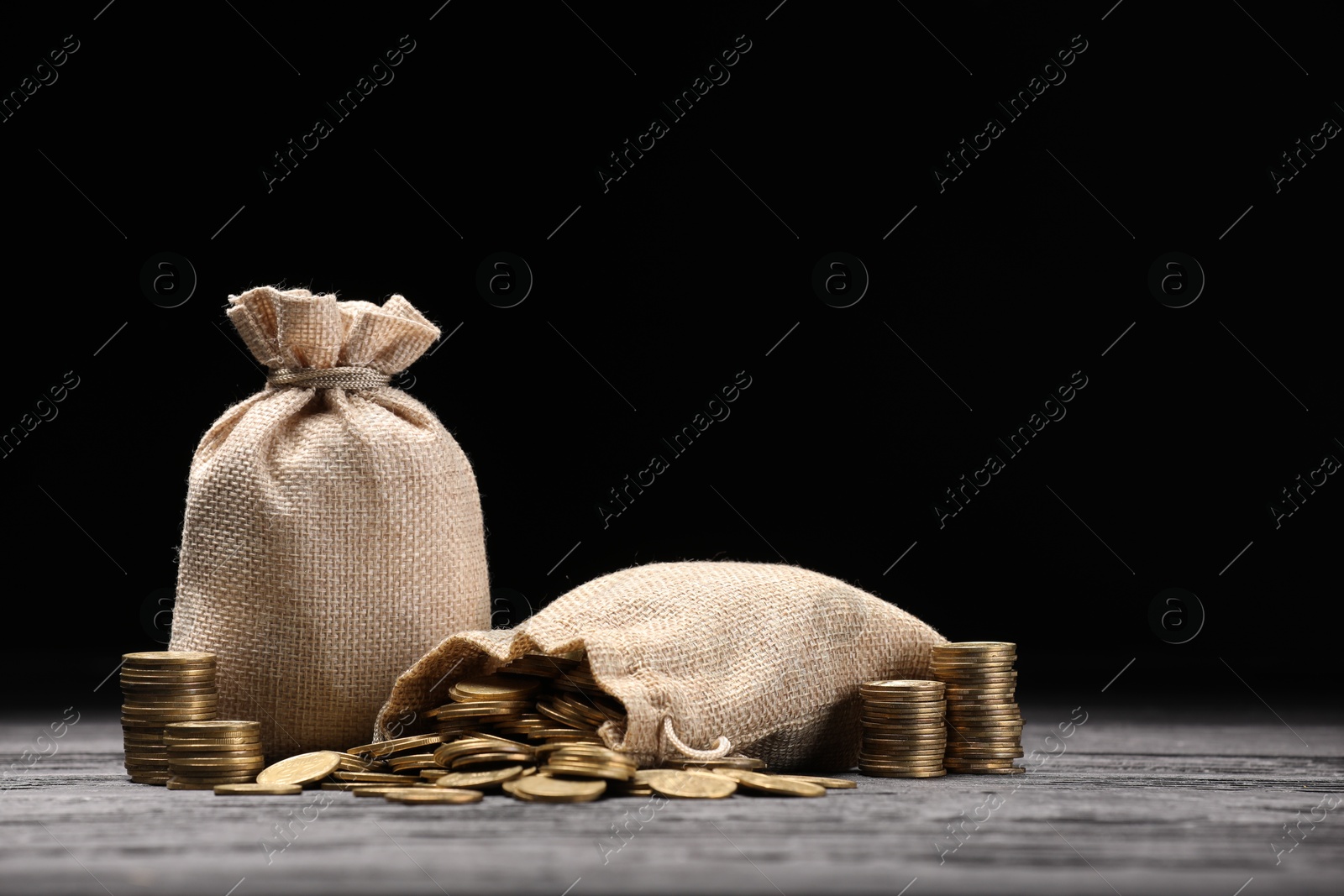 Bags and coins on gray wooden table against dark background Photo of Bags and coins on gray wooden table against dark background
