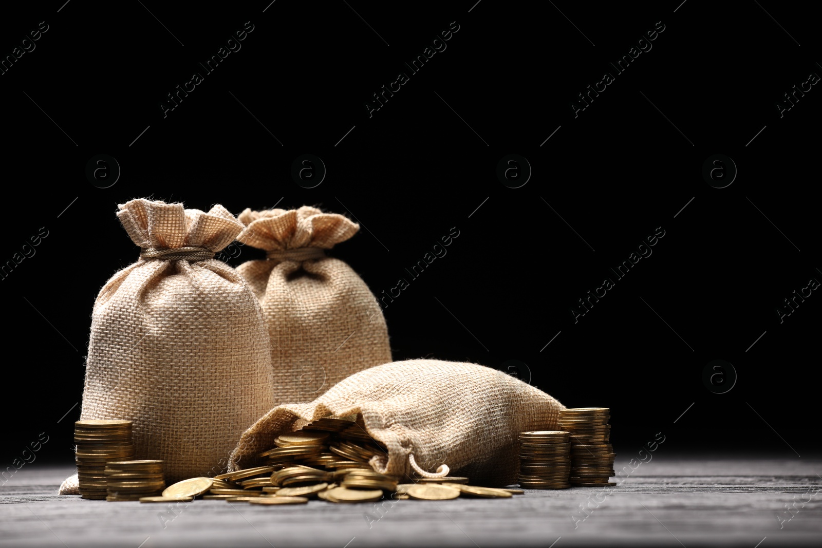 Bags and coins on gray table against dark background Photo of Bags and coins on gray table against dark background