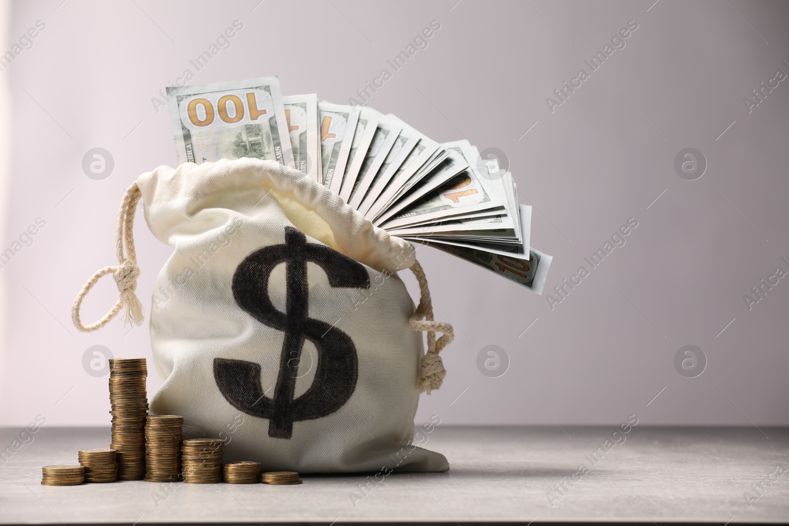 Bag with dollar banknotes and stacked coins on gray table textured against light background, space for text Photo of Bag with dollar banknotes and stacked coins on gray table textured against light background, space for text