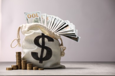 Photo of Bag with dollar banknotes and stacked coins on gray table textured against light background, space for text