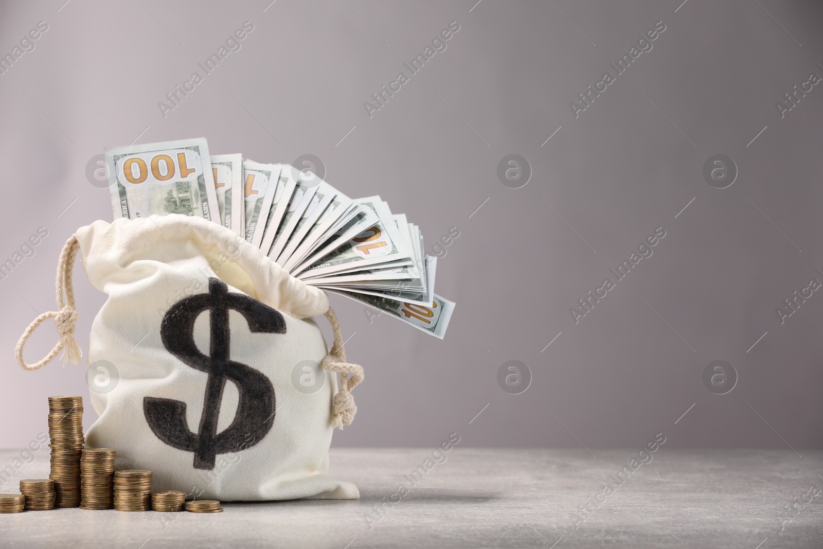 Bag with dollar banknotes and stacked coins on gray table textured against light background, space for text Photo of Bag with dollar banknotes and stacked coins on gray table textured against light background, space for text