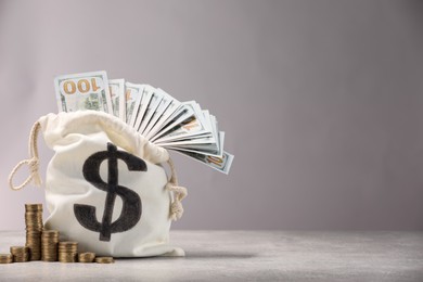 Photo of Bag with dollar banknotes and stacked coins on gray table textured against light background, space for text