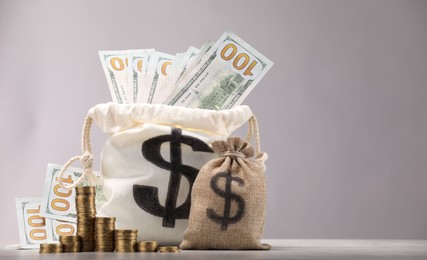 Photo of Bag with dollar banknotes and stacked coins on gray table against light background, space for text