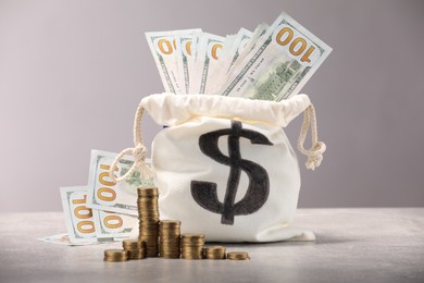 Photo of Bag with dollar banknotes and stacked coins on gray table textured against light background