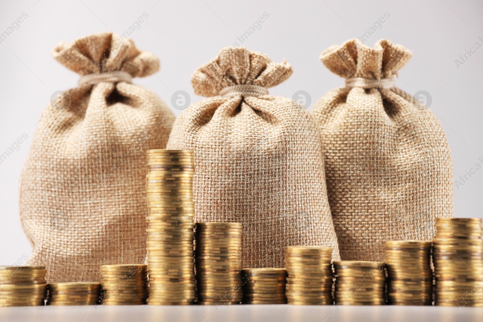 Bags and stacked coins on light background, closeup Photo of Bags and stacked coins on light background, closeup