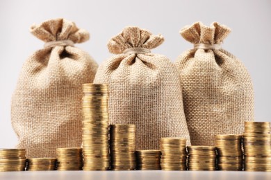 Photo of Bags and stacked coins on light background, closeup