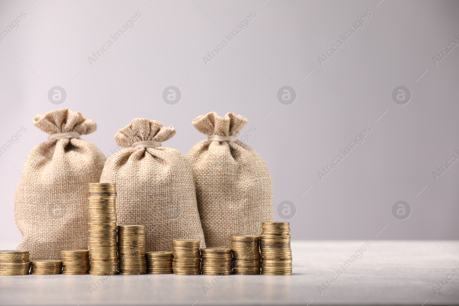 Bags and stacked coins on gray table against light background, space for text Photo of Bags and stacked coins on gray table against light background, space for text