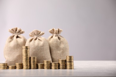 Photo of Bags and stacked coins on gray table against light background, space for text