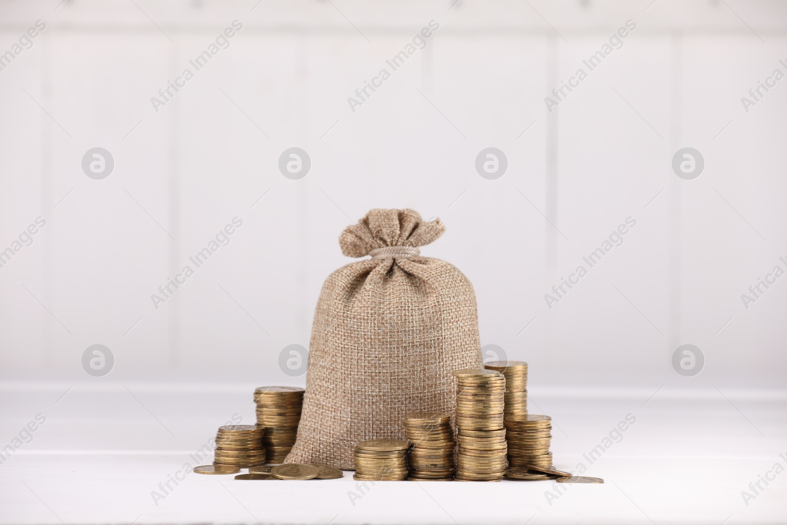 Bag and stacked coins on white table against light background Photo of Bag and stacked coins on white table against light background