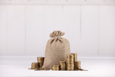 Photo of Bag and stacked coins on white table against light background