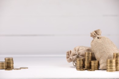 Photo of Bags and stacked coins on white table against light background, space for text