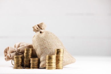 Photo of Bags and stacked coins on white table against light background, space for text