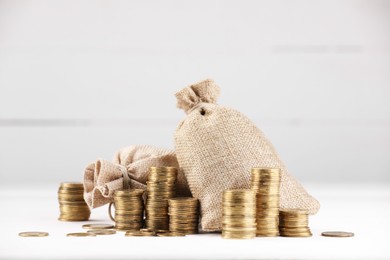Photo of Bags and stacked coins on white table against light background