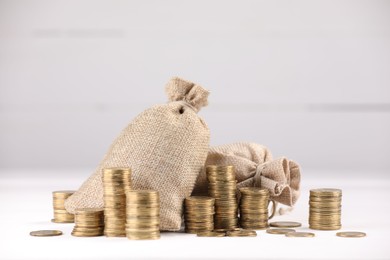 Photo of Bags and stacked coins on white table against light background