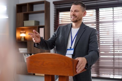 Photo of Man giving public speech with microphone at lectern indoors