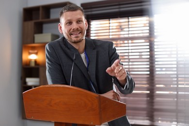 Photo of Man giving public speech with microphone at lectern indoors