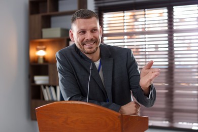 Photo of Man giving public speech with microphone at lectern indoors