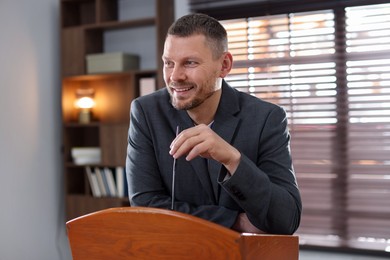 Photo of Man giving public speech with microphone at lectern indoors
