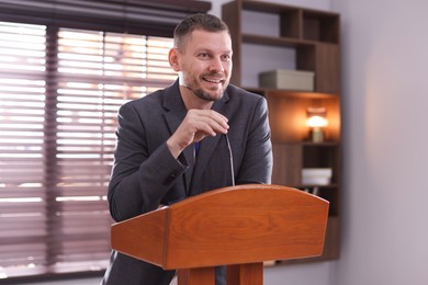 Photo of Man giving public speech with microphone at lectern indoors