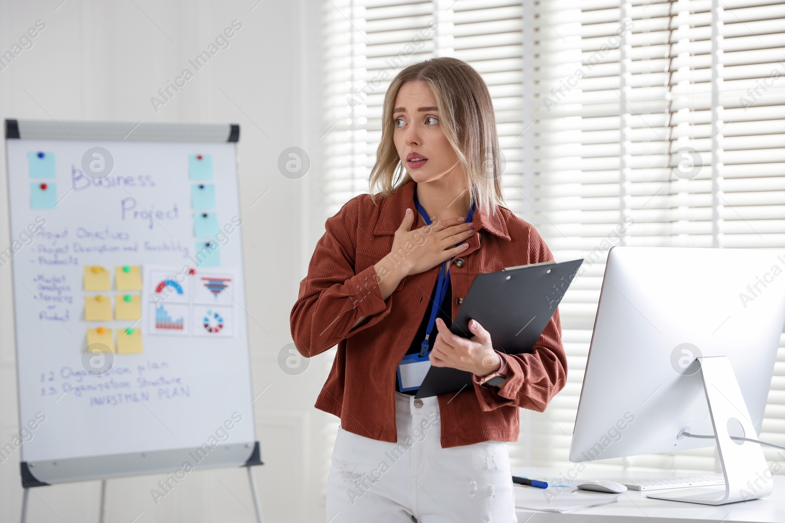 Photo of Fear of public speaking. Nervous woman with clipboard indoors