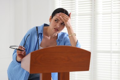 Photo of Fear of public speaking. Nervous woman with microphone at lectern indoors
