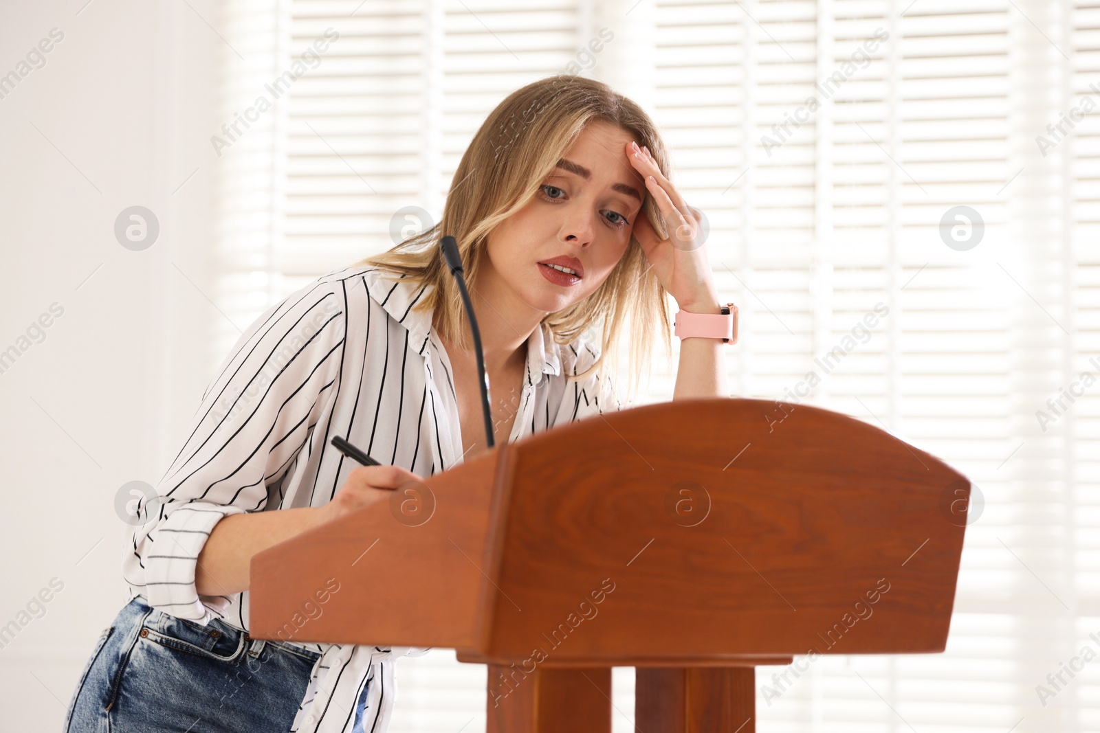 Photo of Fear of public speaking. Nervous woman with microphone at lectern indoors