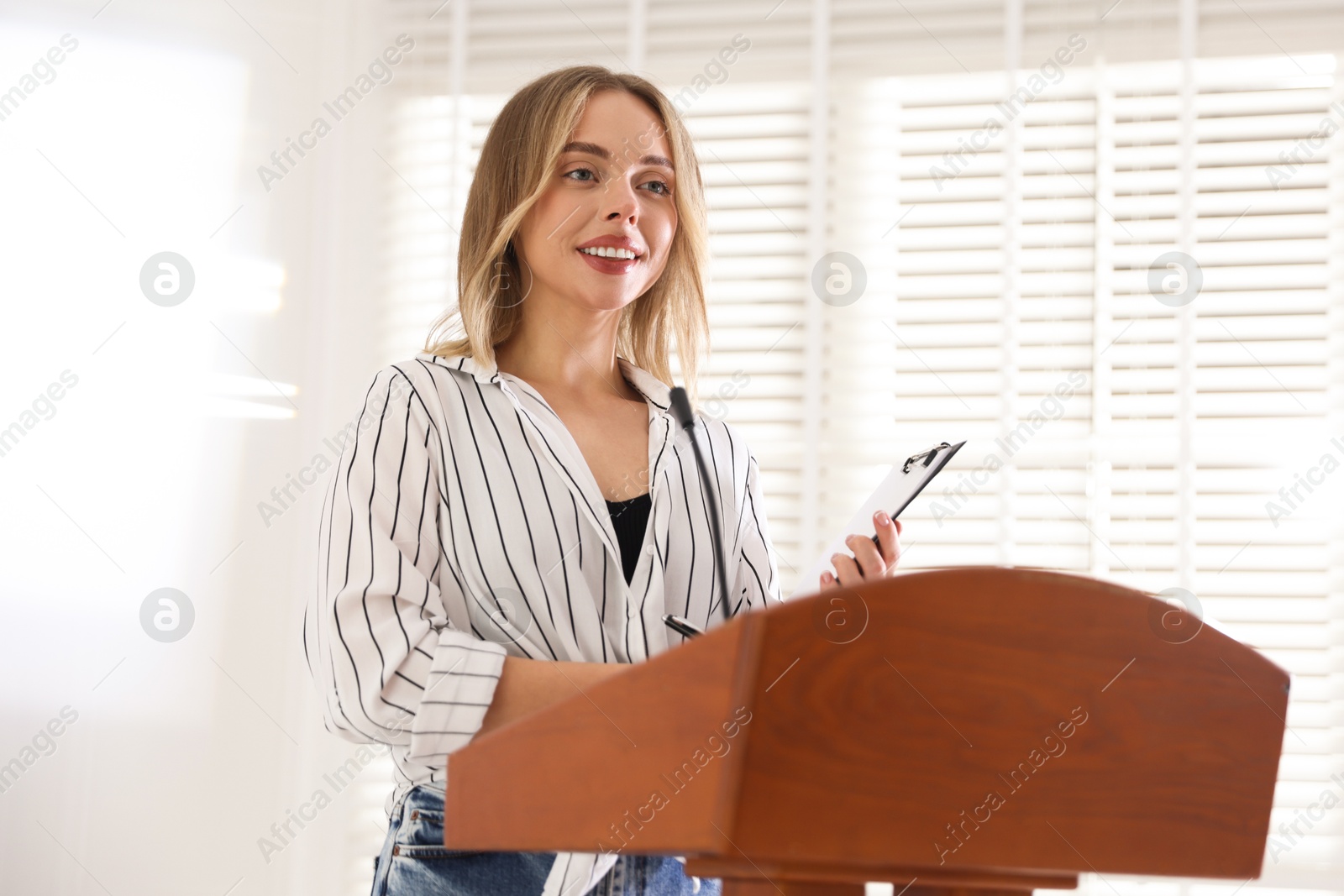 Photo of Woman giving public speech with microphone at lectern indoors