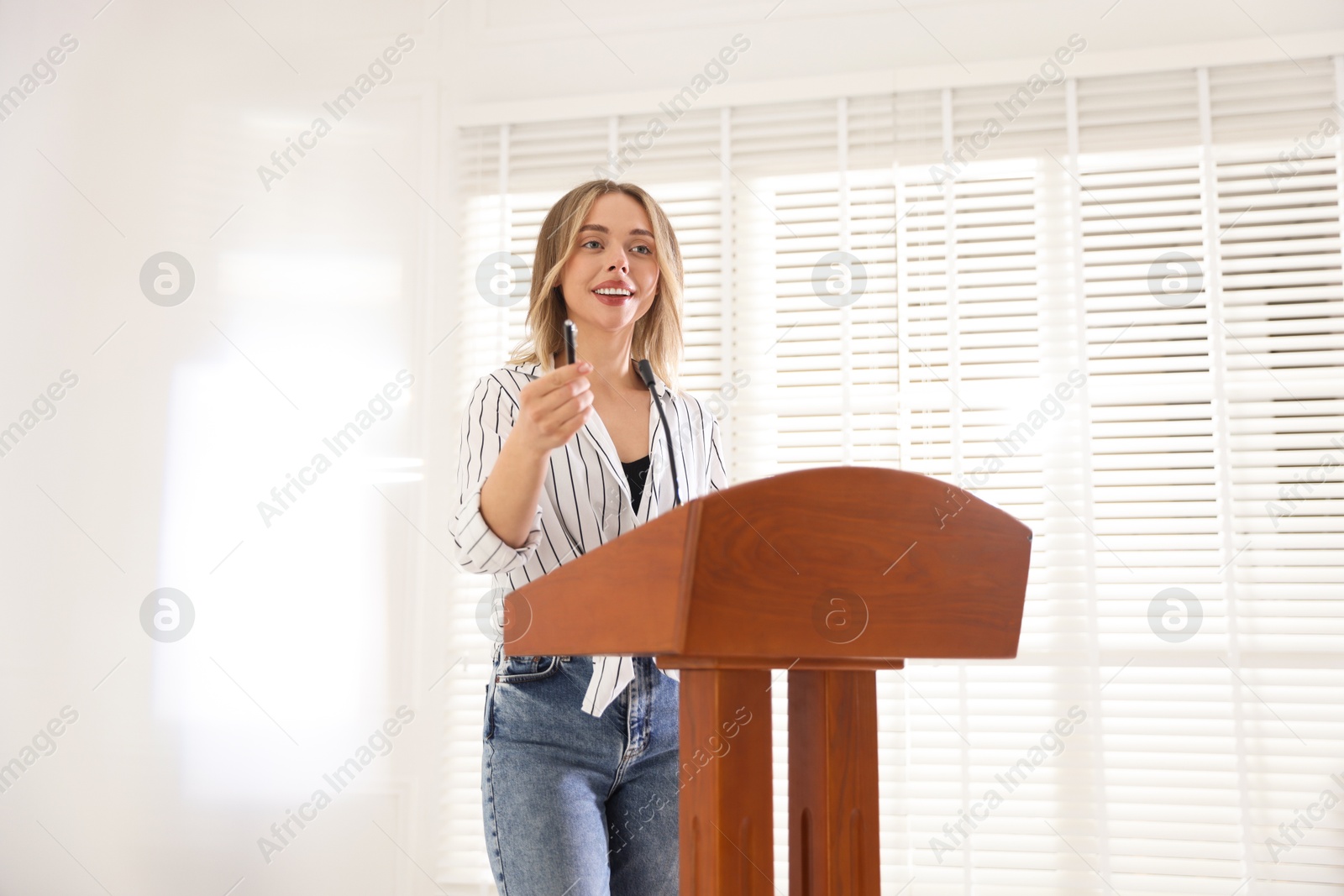 Photo of Woman giving public speech with microphone at lectern indoors