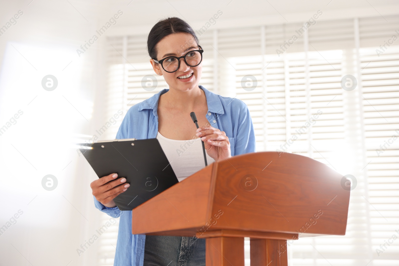 Photo of Woman giving public speech with microphone at lectern indoors