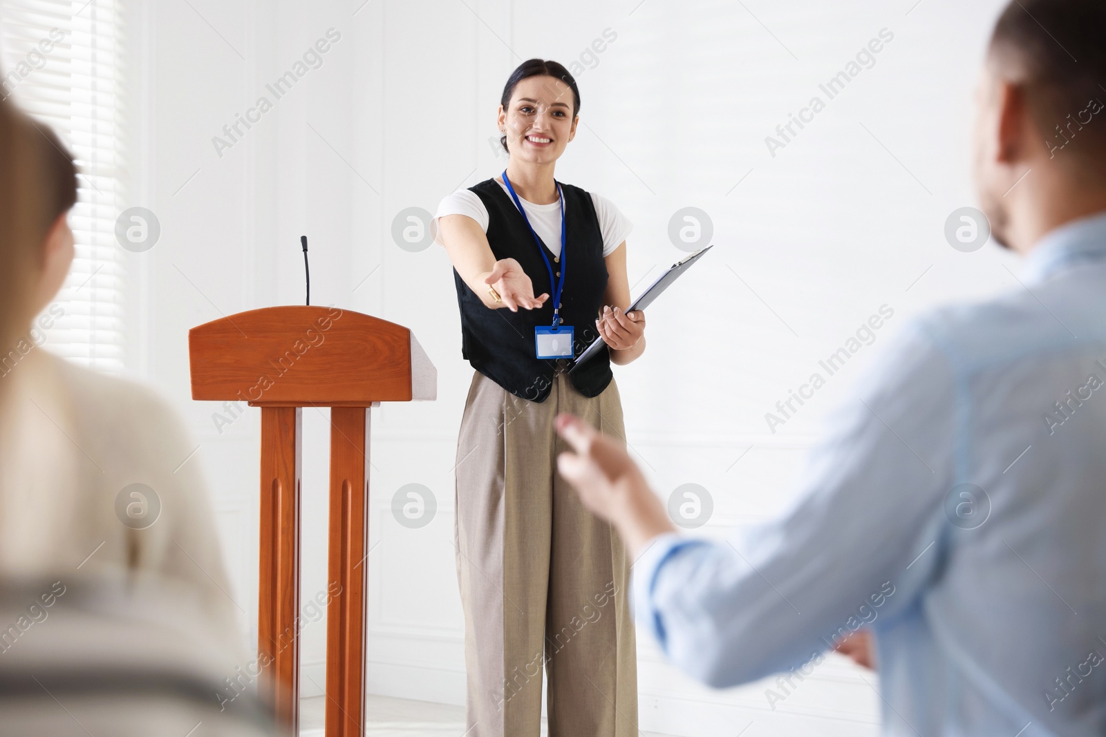 Photo of Woman giving public speech at lectern in front of audience indoors