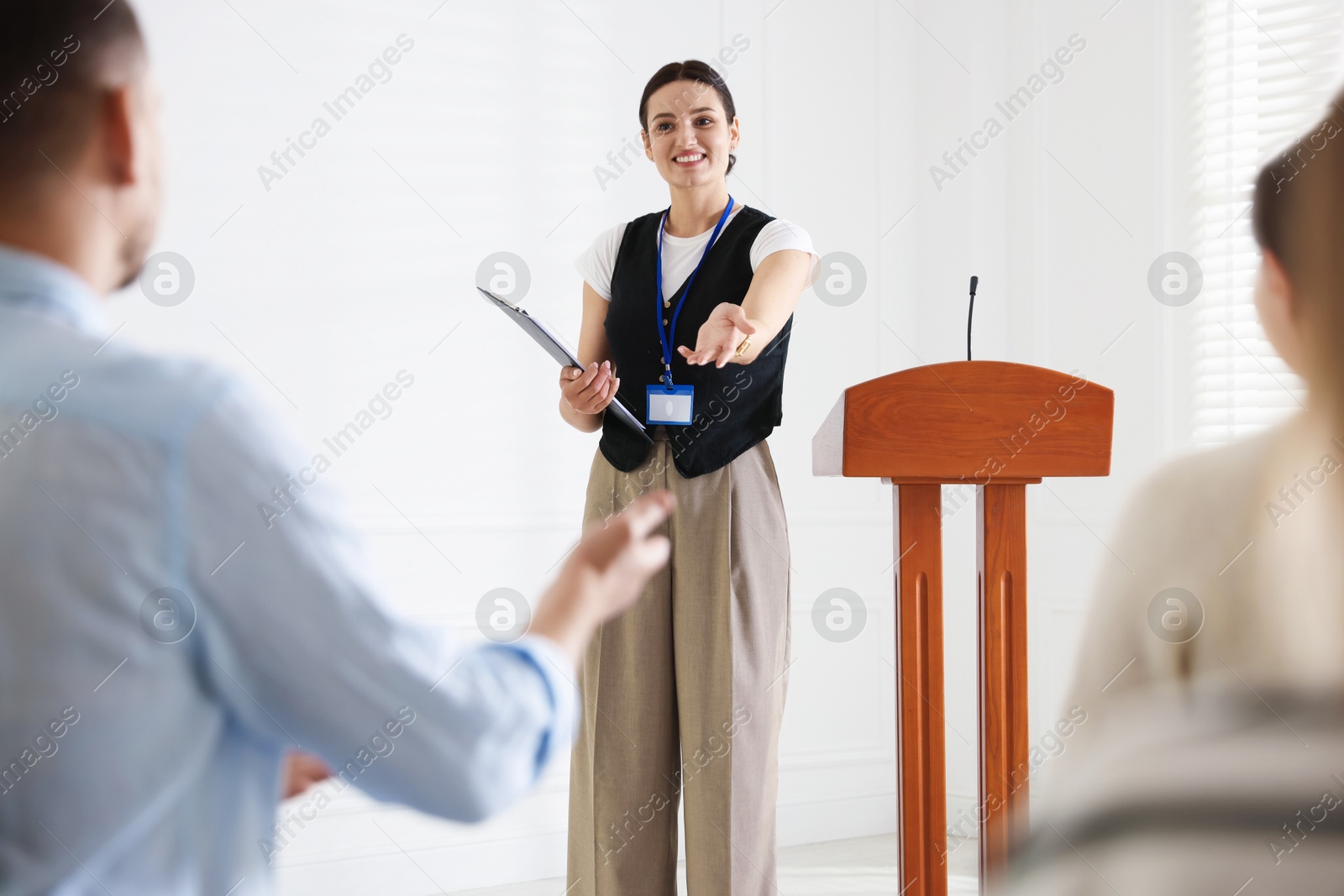Photo of Woman giving public speech at lectern in front of audience indoors