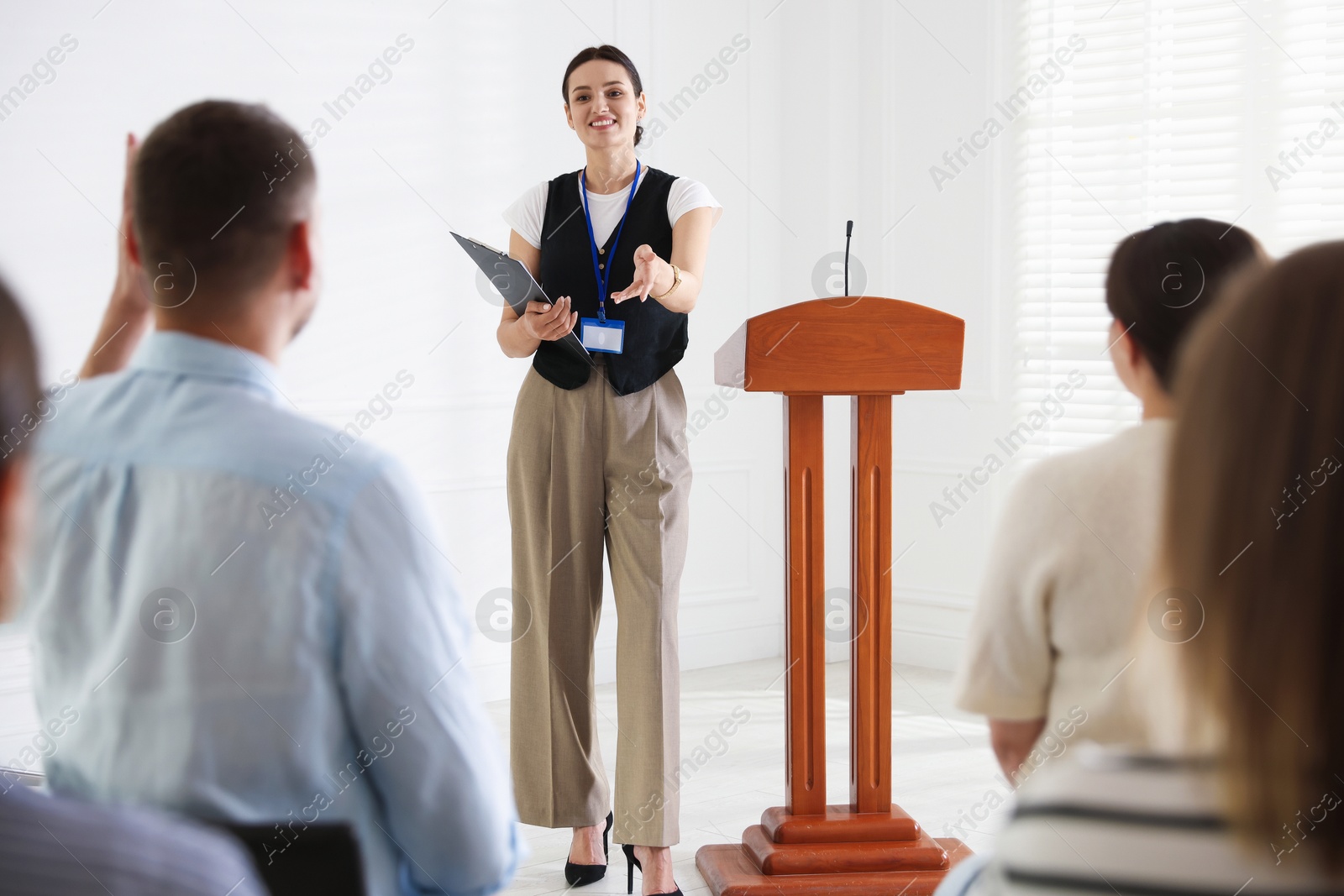 Photo of Woman giving public speech at lectern in front of audience indoors