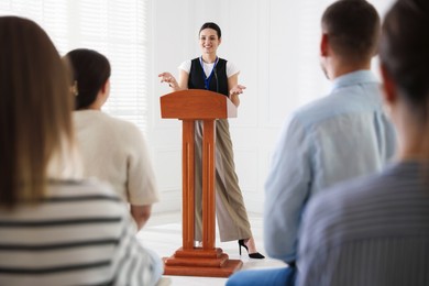 Photo of Woman giving public speech at lectern in front of audience indoors