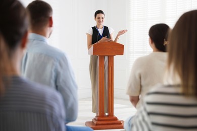Photo of Woman giving public speech at lectern in front of audience indoors