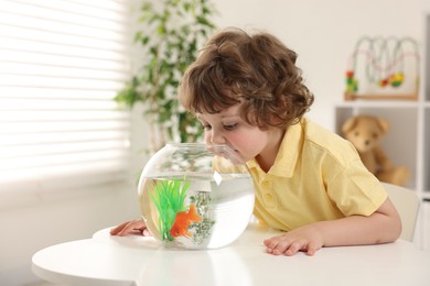 Photo of Little boy with goldfish in aquarium on table at home