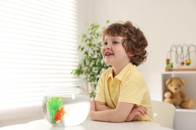 Photo of Little boy with goldfish in aquarium on table at home. Space for text
