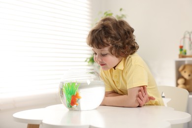 Photo of Little boy with goldfish in aquarium on table at home. Space for text