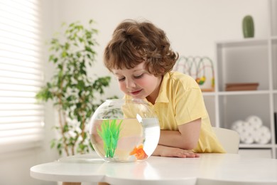 Photo of Little boy with goldfish in aquarium on table at home