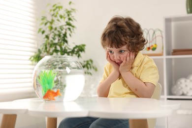 Photo of Little boy with goldfish in aquarium making wish at home