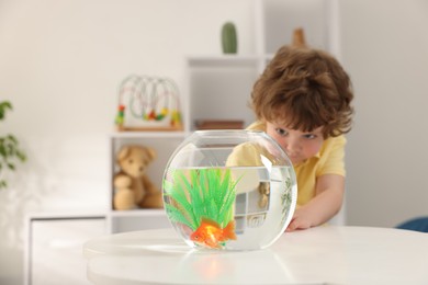 Photo of Little boy with goldfish in aquarium on table at home. Space for text