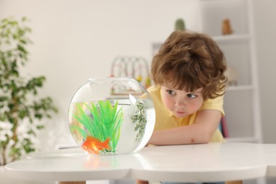 Photo of Little boy with goldfish in aquarium on table at home