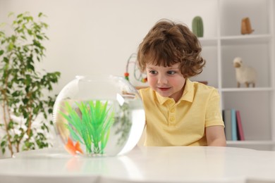 Photo of Little boy with goldfish in aquarium on table at home
