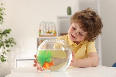Photo of Little boy with goldfish in aquarium on table at home
