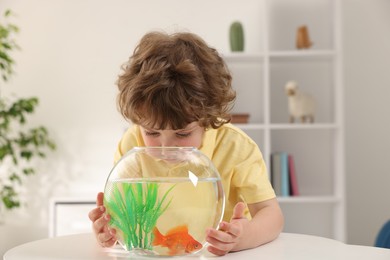 Photo of Little boy with goldfish in aquarium on table at home